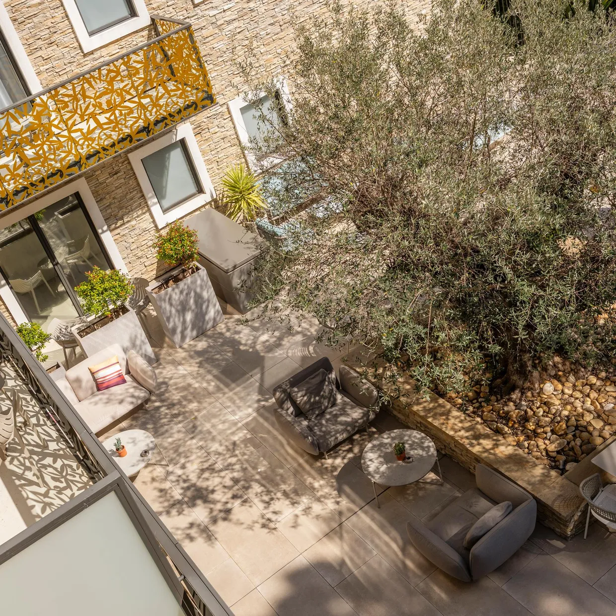 Terrasse avec mobilier de jardin, table, chaises et canapé, entourée de végétation et de murs en briques avec des motifs décoratifs