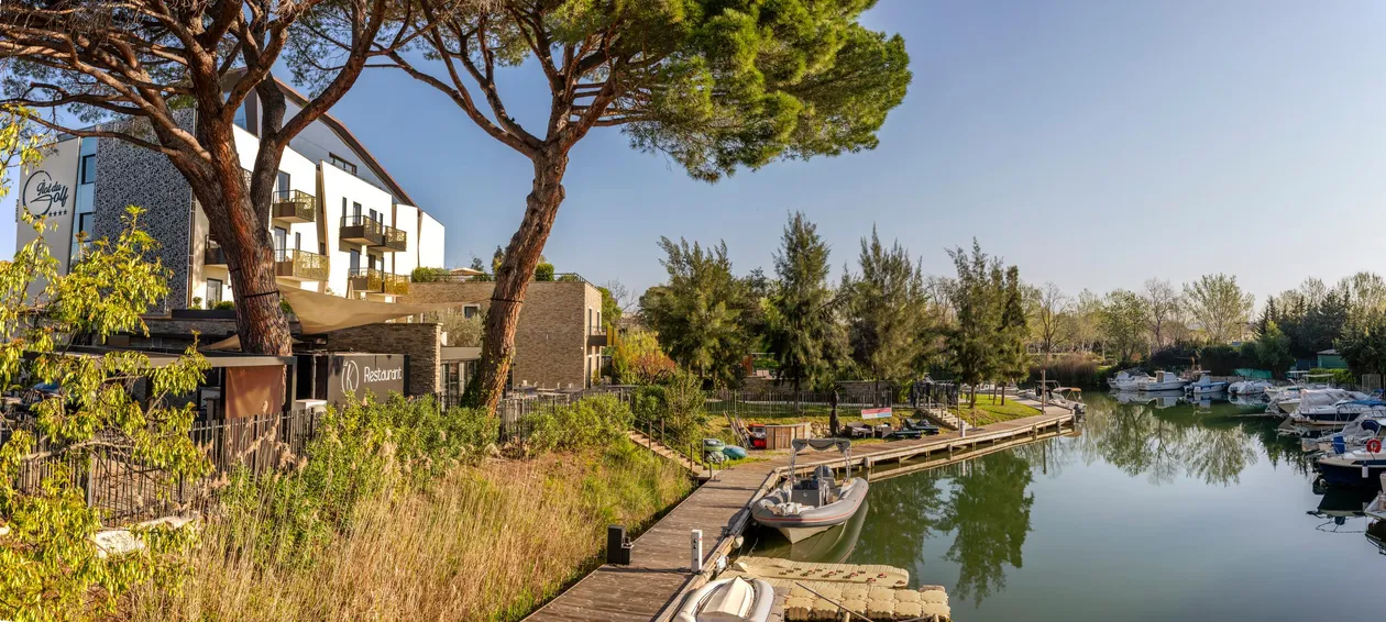 Un hôtel et un restaurant bordent un canal avec des bateaux amarrés, entourés d'arbres et de végétation