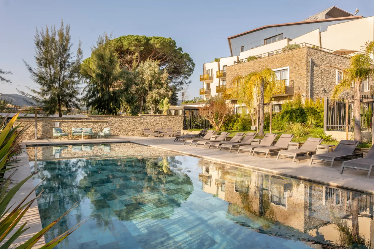 Piscine entourée de transats avec un bâtiment en pierre et des arbres en arrière-plan