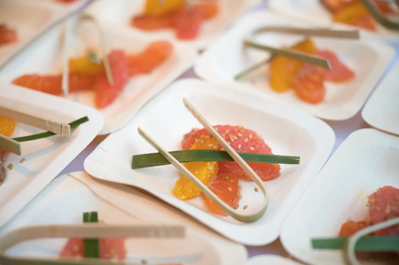 Petits plats en carton contenant des morceaux de fruits et des bâtonnets, disposés sur une nappe à motifs