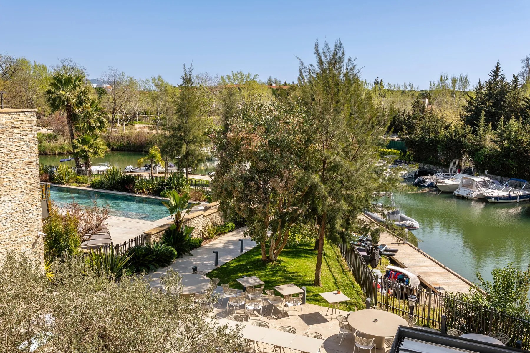 Vue d'un jardin avec des tables et des chaises près d'un plan d'eau où sont amarrés des bateaux