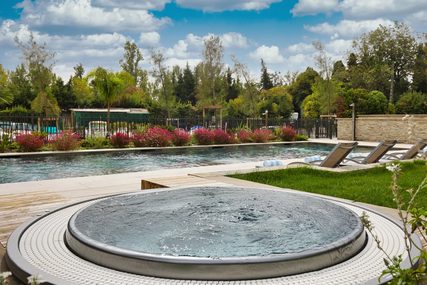 Piscine extérieure entourée de végétation et de fleurs, avec des transats et un petit bassin circulaire au premier plan