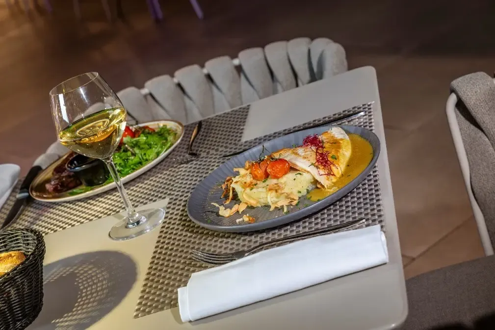 Une table avec une assiette de poisson grillé, une salade, un verre de vin blanc et des couverts