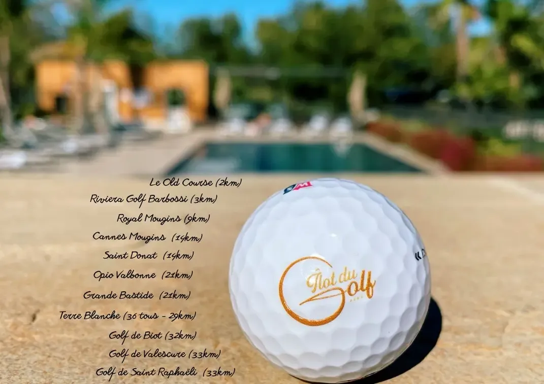 Balle de golf avec l'inscription "Golf du Domaine" devant une piscine et des bâtiments en arrière-plan