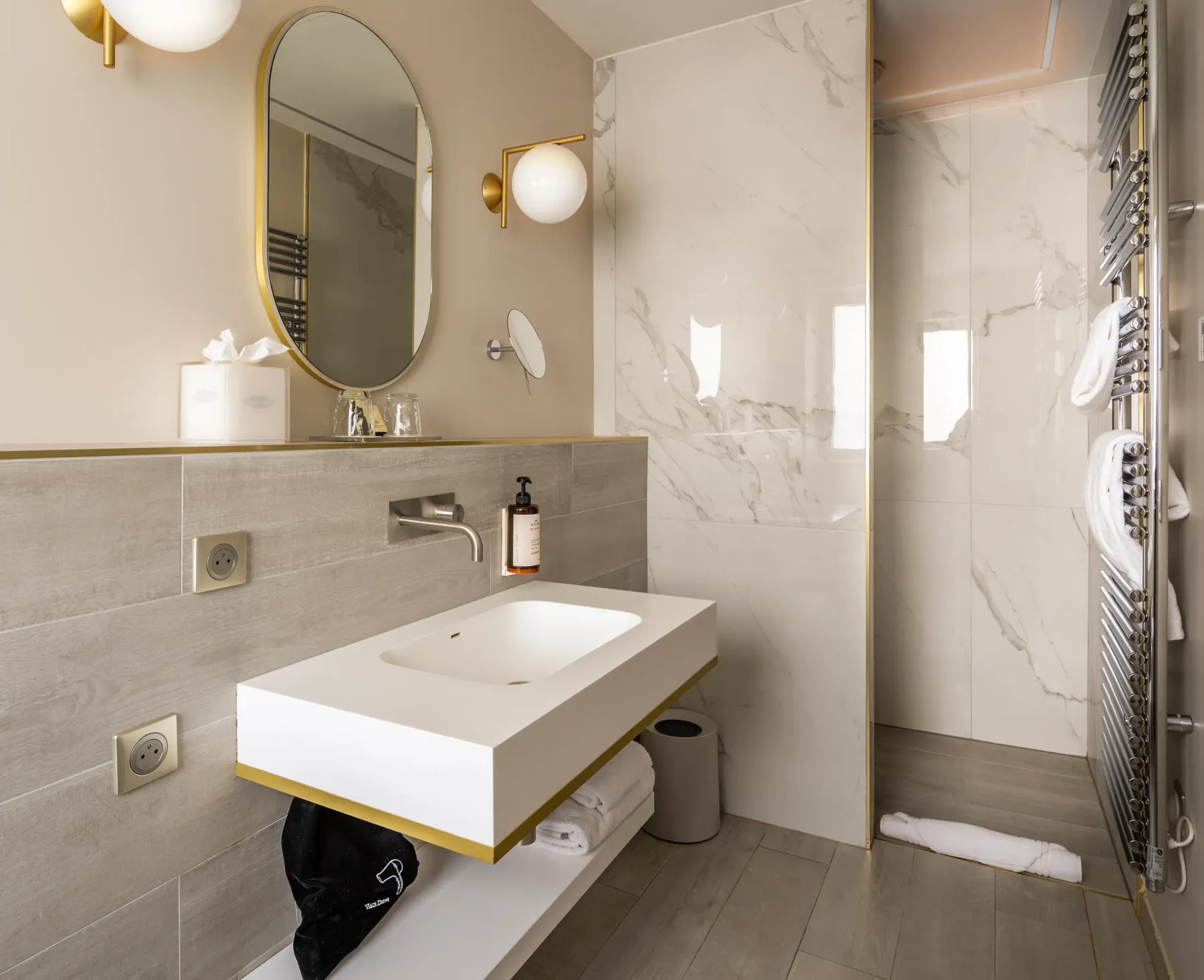 Salle de bain moderne avec lavabo suspendu, miroir ovale, douche à la porte vitrée et accessoires en métal