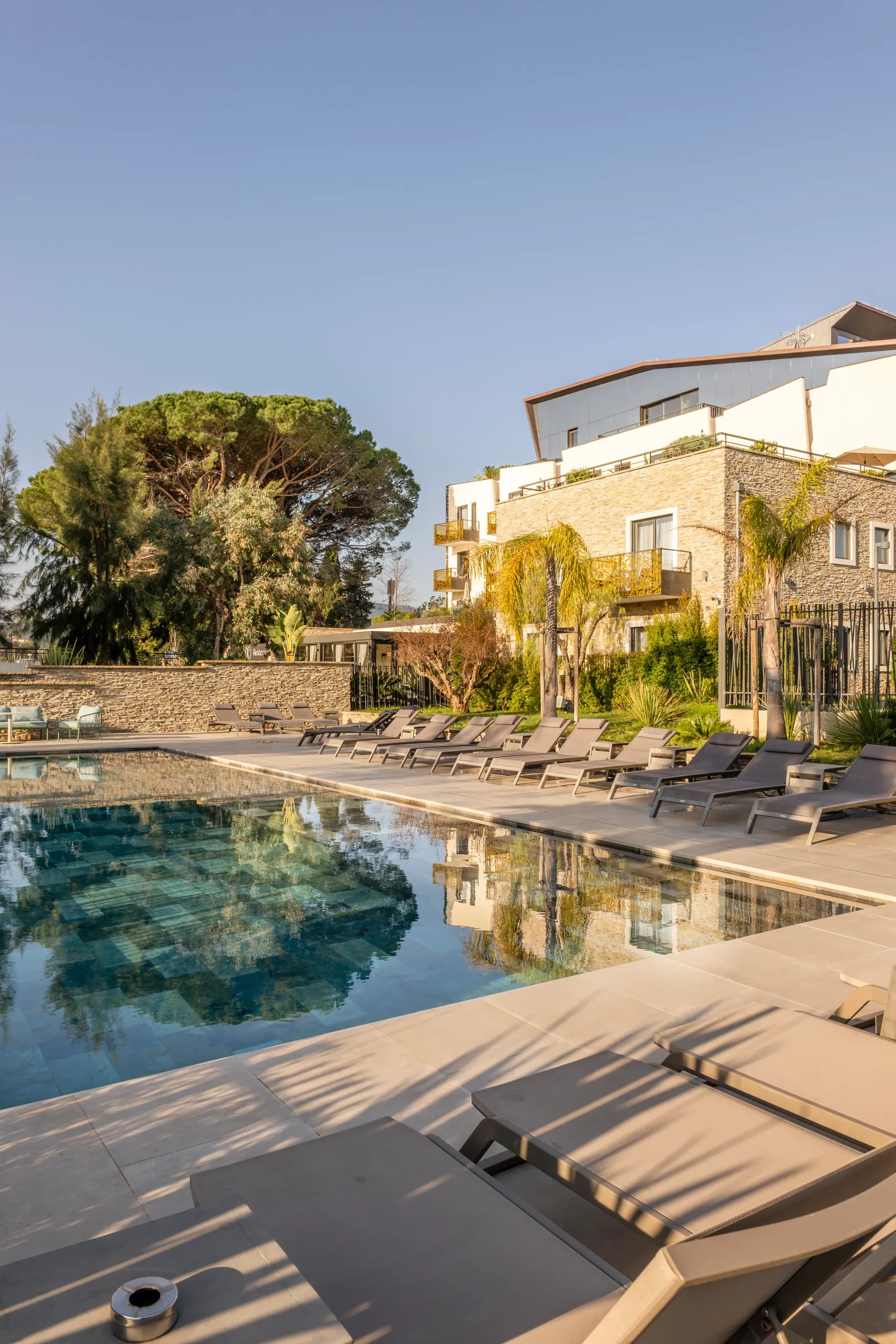 Piscine entourée de transats avec un bâtiment en pierre et des arbres en arrière-plan