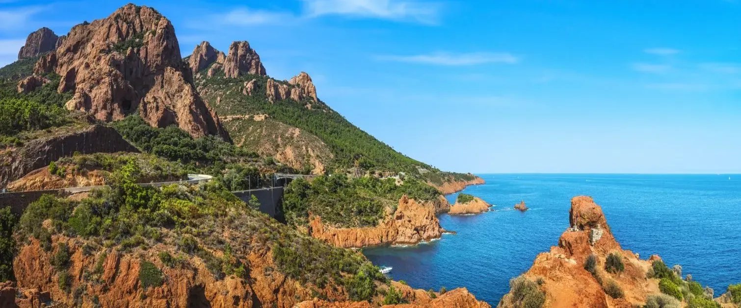 Une côte rocheuse avec des formations montagneuses escarpées et une route sinueuse longeant la mer bleue sous un ciel dégagé