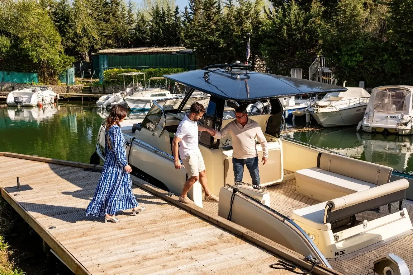 Trois personnes montent sur un bateau amarré à un ponton en bois près d'autres embarcations
