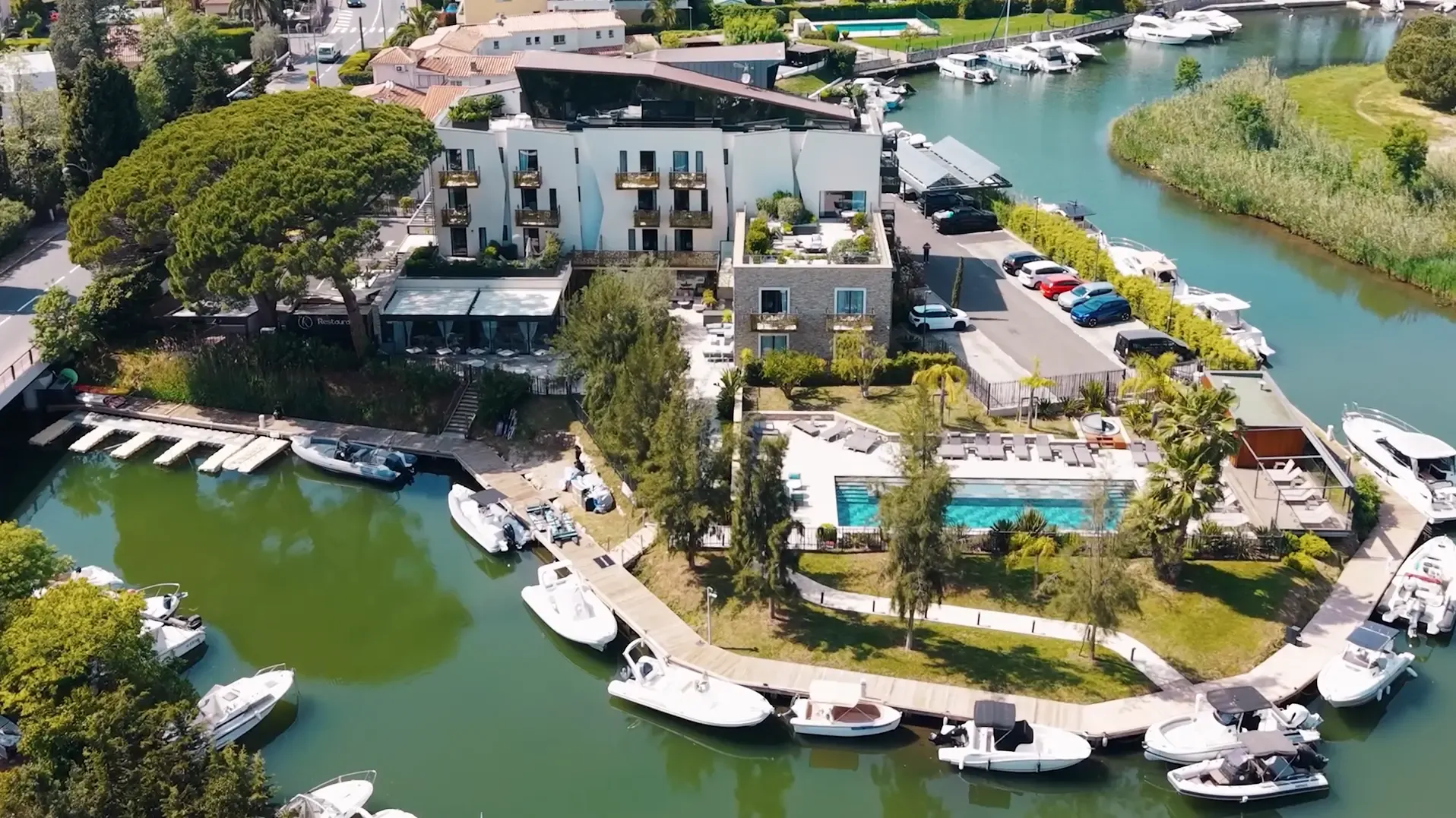 Vue aérienne d'un complexe hôtelier avec piscine et marina, entouré d'eau et de bateaux amarrés